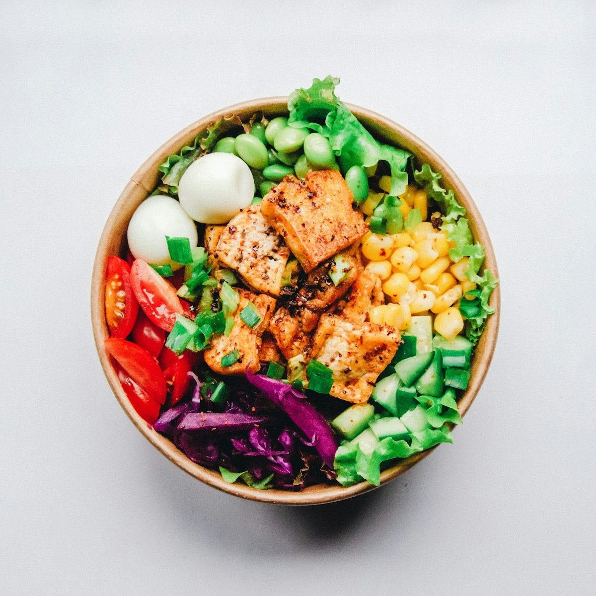 A protein bowl with grilled paneer, egg, corn, cucumber and greens